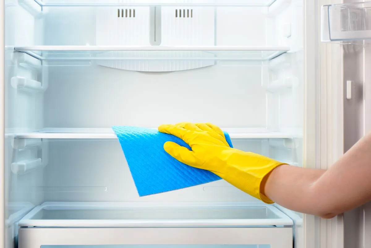 Уборка внутри холодильника синей тряпкой в ​​желтых резиновых перчатках