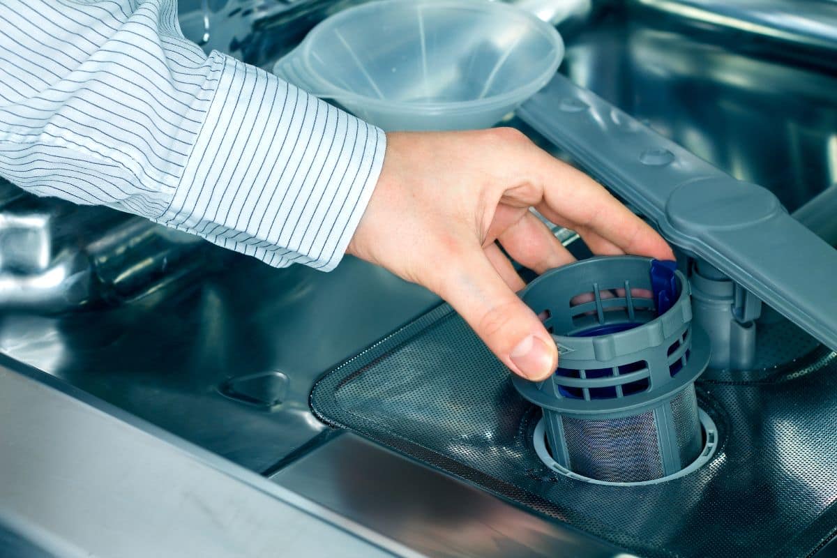 Мужская рука в полосатой рубашке достает посудомоечную машину из посудомоечной машины
